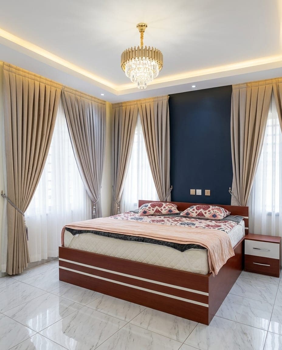 Taupe drapes and sheers framing bedroom windows under a crystal chandelier